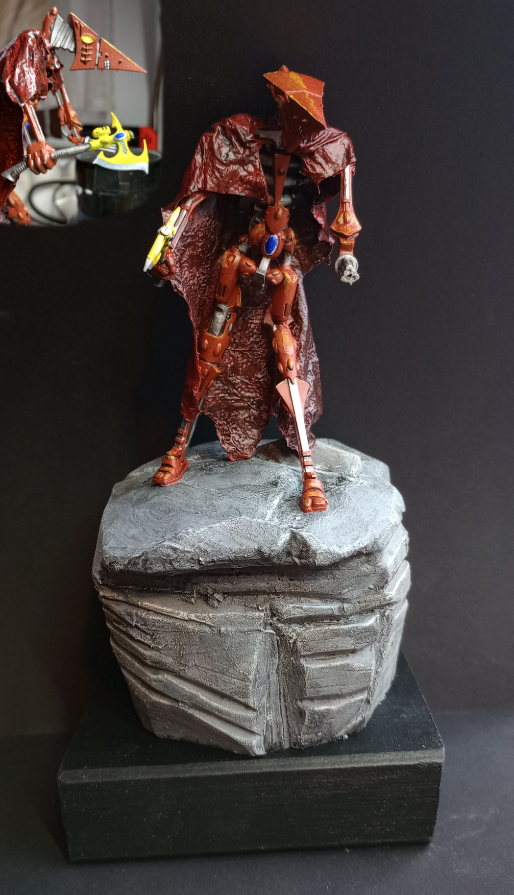 A red robot with a cape standing on a boulder.